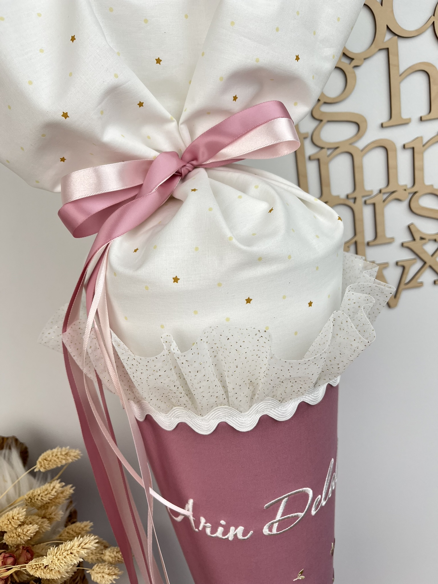 Detailansicht Verschluss aus cremeweißem Stoff mit goldenen Sternchen, Satinbändern und Glitzertüll-Rüsche
